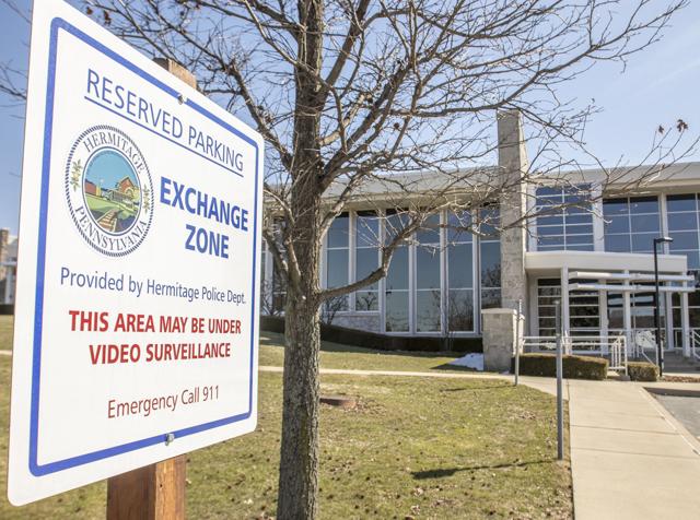 image of a save exchange zone in a police station parking lot with sign reading reserved parking exchange zone this area may be under video surveillance emergency call 911